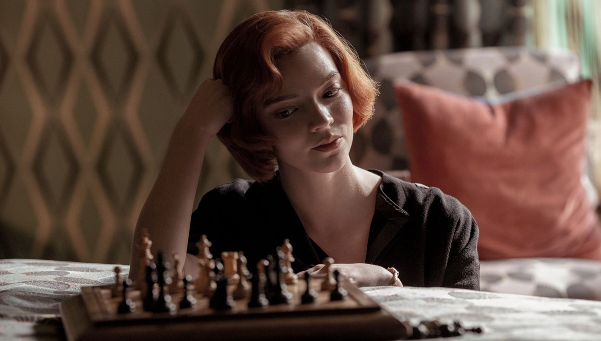 Photo of actress Anya Taylor Joy from The Queen’s Gambit in front of a chess set. She is looking at the pieces.